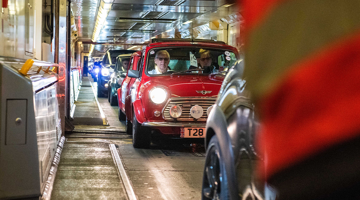 Long queue of Mini cars driven onto a train carriage ready to depart on a journey red mini with two passengers inside at the front